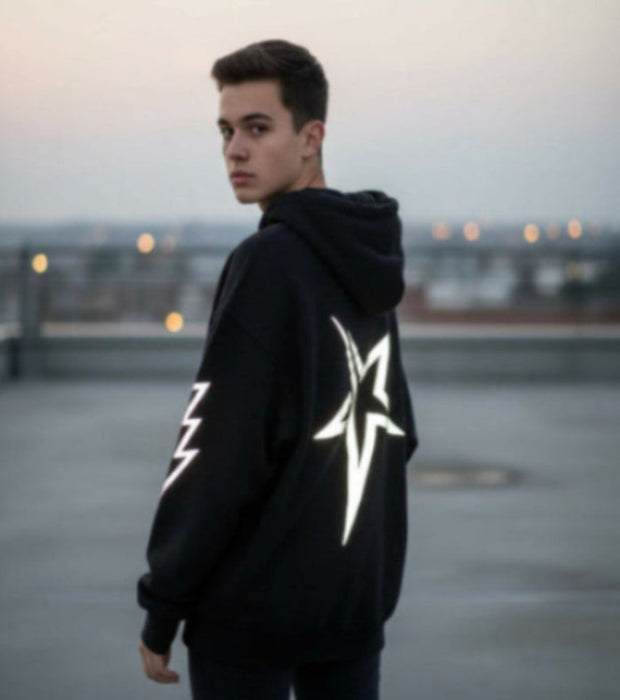 Person wearing a black hoodie with reflective designs on a rooftop at dusk.