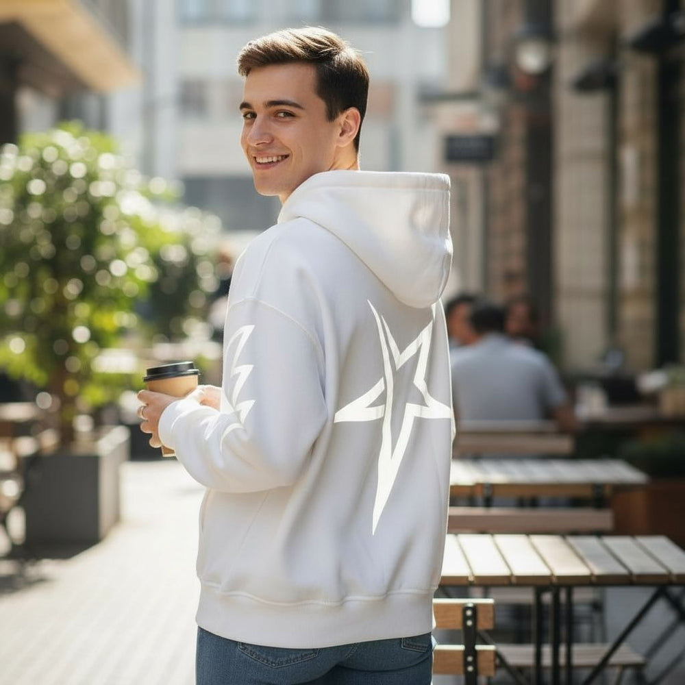 Man wearing a white hoodie with a star design, holding a coffee cup, on a city street.