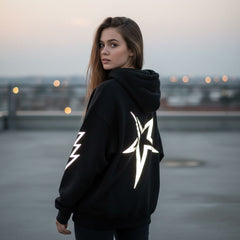 Person wearing a black hoodie with reflective designs on a rooftop at dusk.
